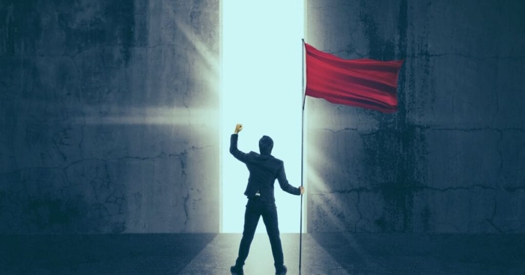 Person in a suit triumphantly raises a red flag in front of a glowing door, symbolizing success and new beginnings.