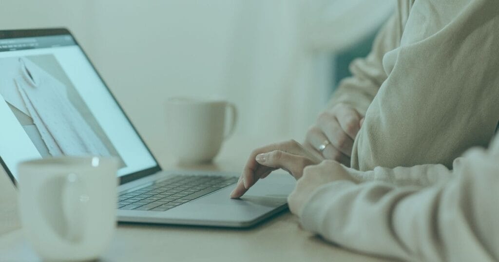Person browsing an online clothing store on a laptop, with coffee cups on the table.