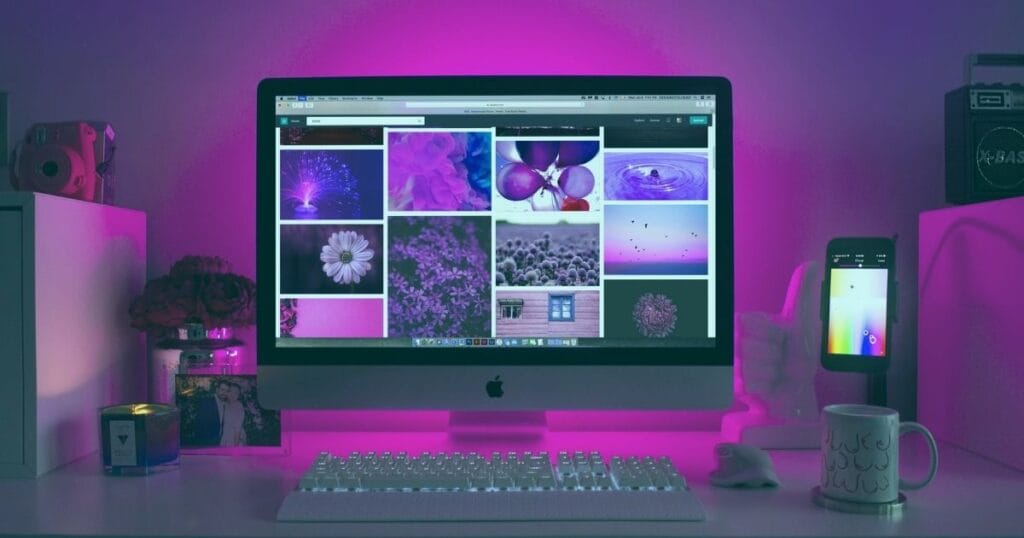 A purple-themed workspace featuring an iMac displaying floral images, a smartphone, and a candle on the desk.