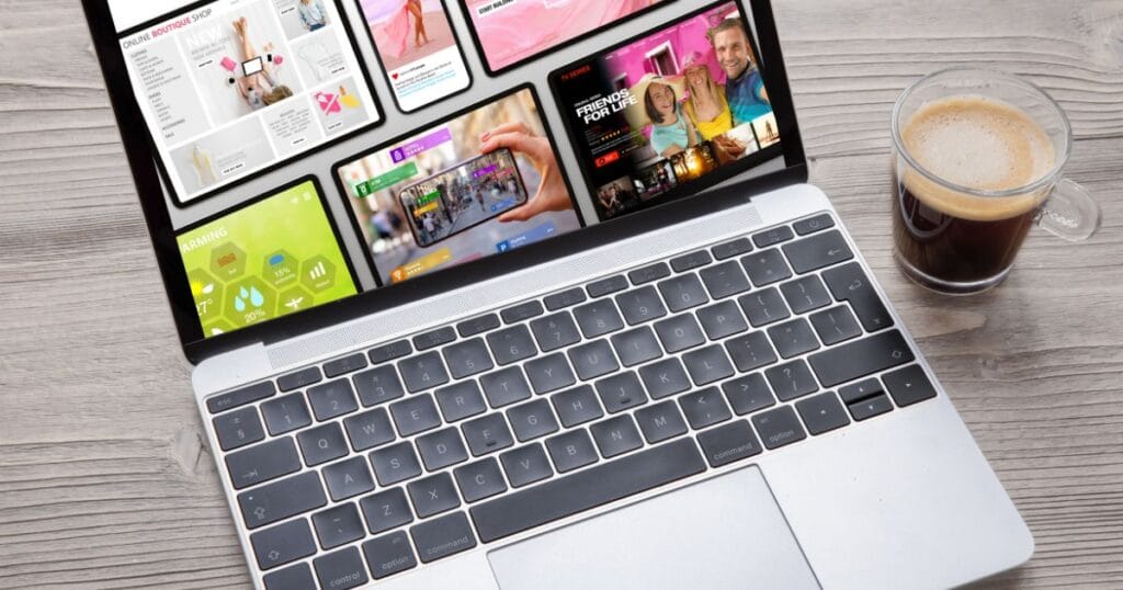 A laptop displaying colorful app interfaces and a smartphone, with a cup of coffee nearby on a wooden table.