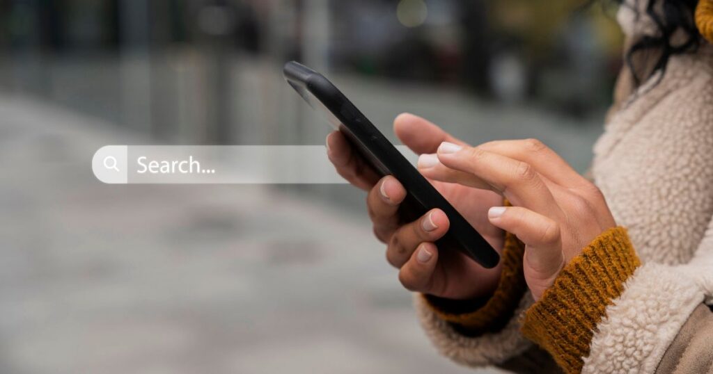 A person using a smartphone to search online, focused on the screen in an outdoor setting.